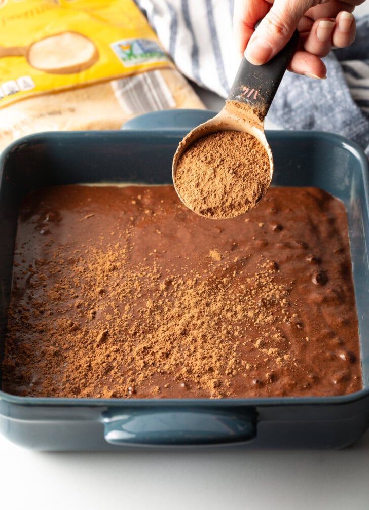 Adding chocolate powder to the cake batter in a pan.