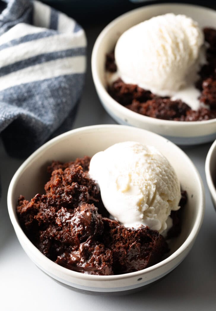 White bowl with serving of chocolate lava cake and a scoop of vanilla ice cream.