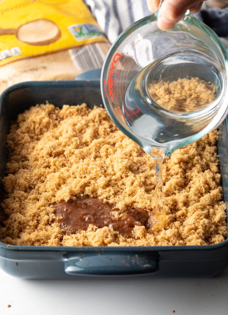 Crumbled brown sugar in a pan, pouring boiling water over the cake.