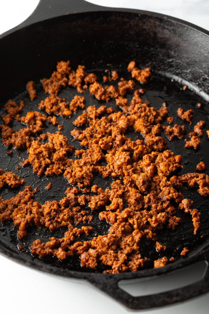 Cooking chorizo crumbled in a black skillet.