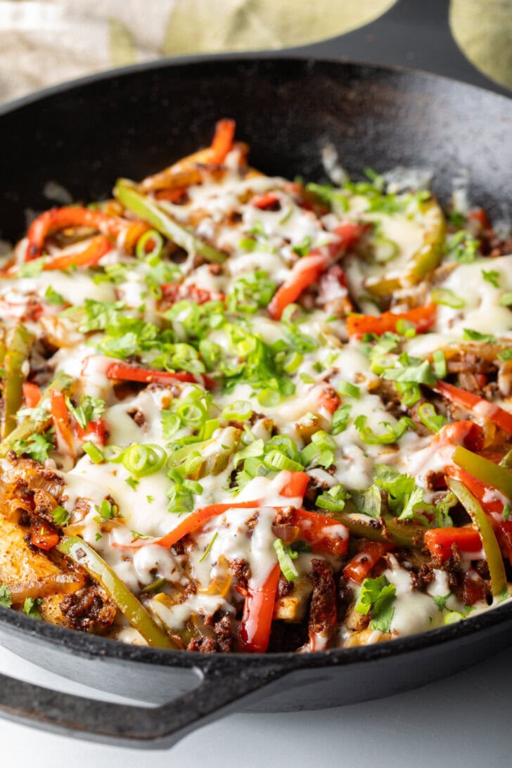 Choripollo in a black skillet, topped with cheese and green onions.