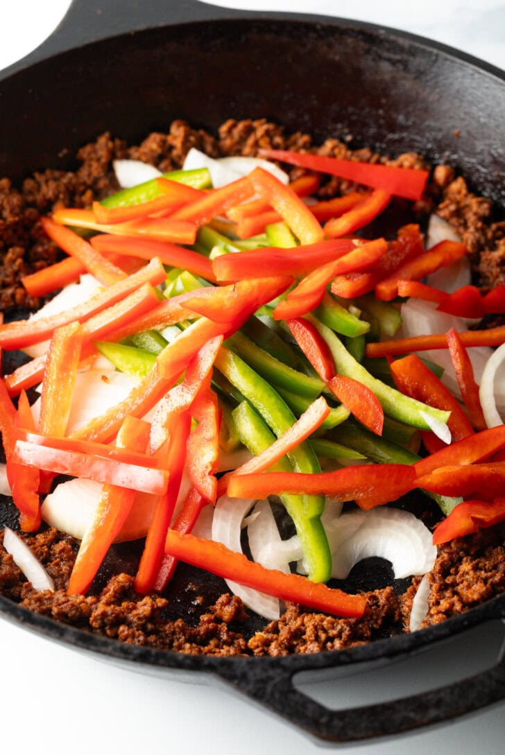 Adding sliced red, green, orange, and yellow bell peppers to the cooked chorizo in the skillet.