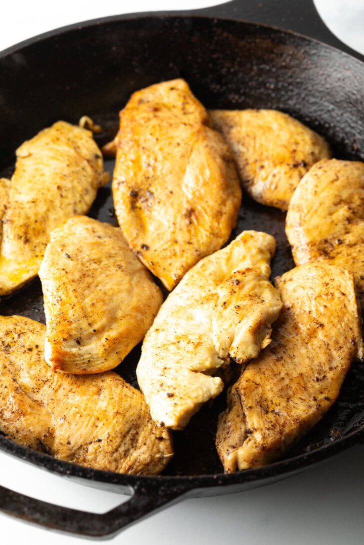 A black skillet with 7 pieces of seared chicken.