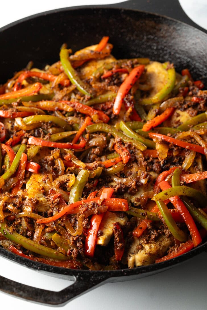 Yellow, green, orange, and red sliced bell peppers in a black skillet with seasonings.