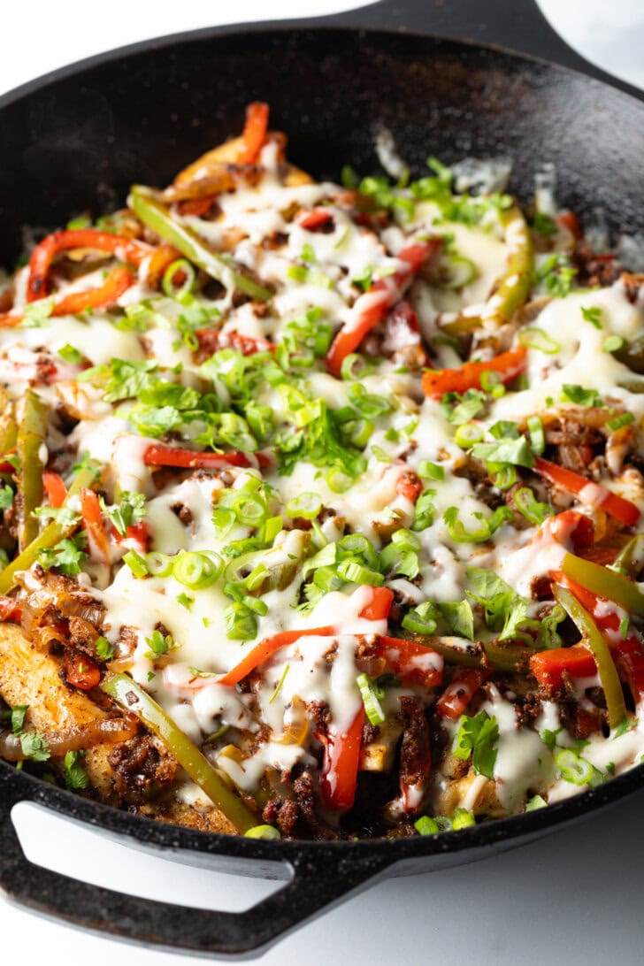 Choripollo in a black skillet, topped with cheese and green onions.