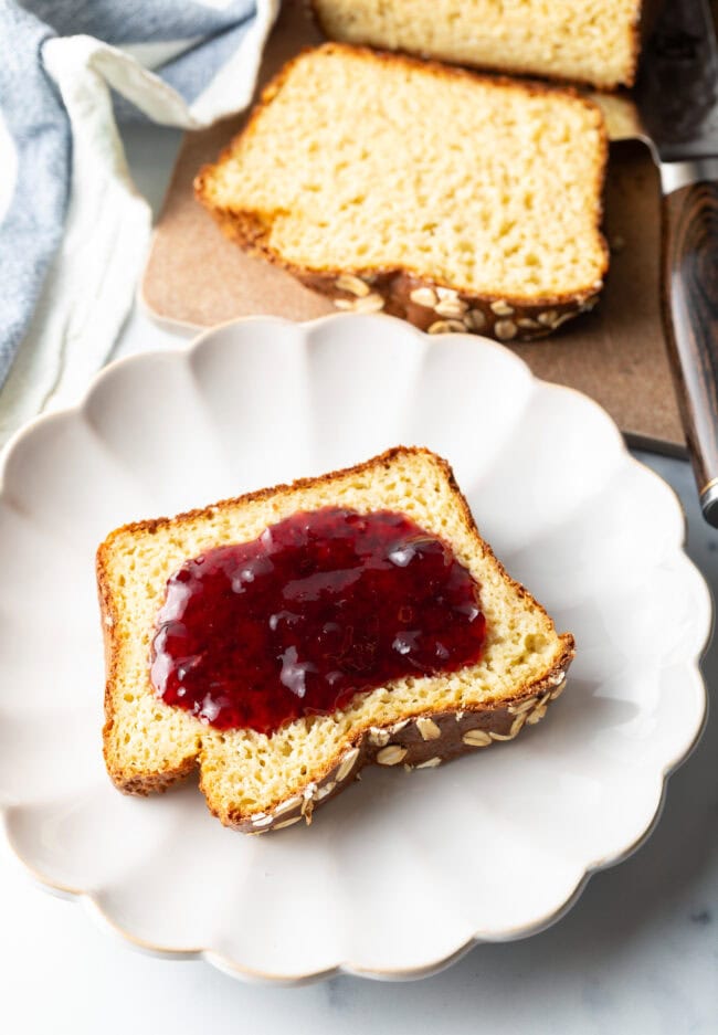 Slice of bread topped with red jelly, on a white plate.