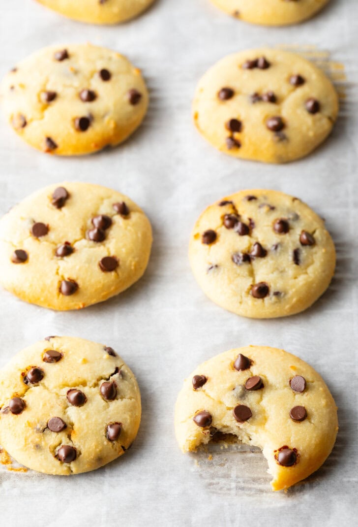 8 cottage cheese chocolate chip cookies cooling on a baking sheet. A front cookie has a bite missing.