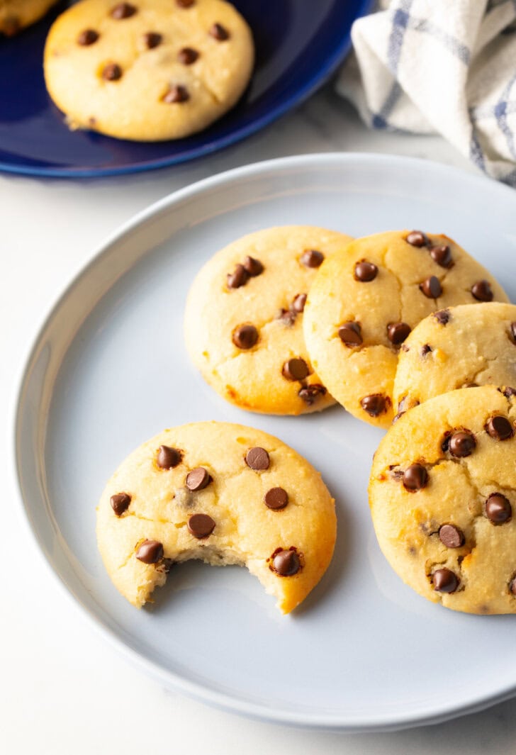 Light blue plate with 6 cookies. One chocolate chip cookie has a bite taken out.