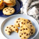 Light blue plate with 6 cookies. One chocolate chip cookie has a bite taken out.