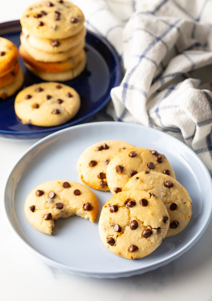 Light blue plate with 6 cookies. One chocolate chip cookie has a bite taken out.