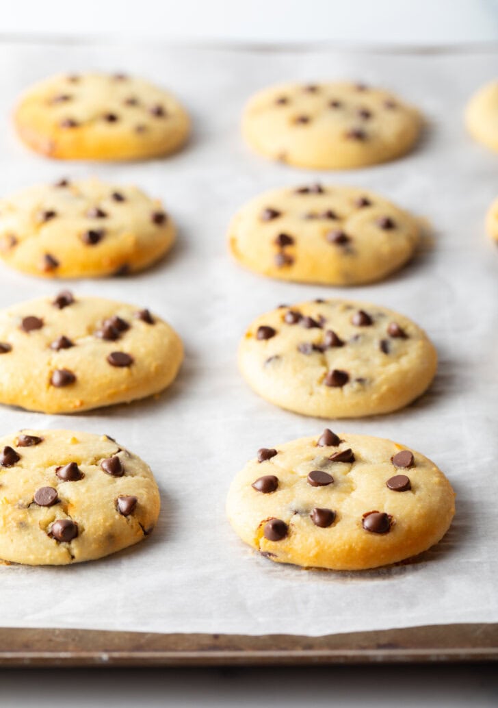 8 cottage cheese chocolate chip cookies cooling on a baking sheet. A front cookie has a bite missing.