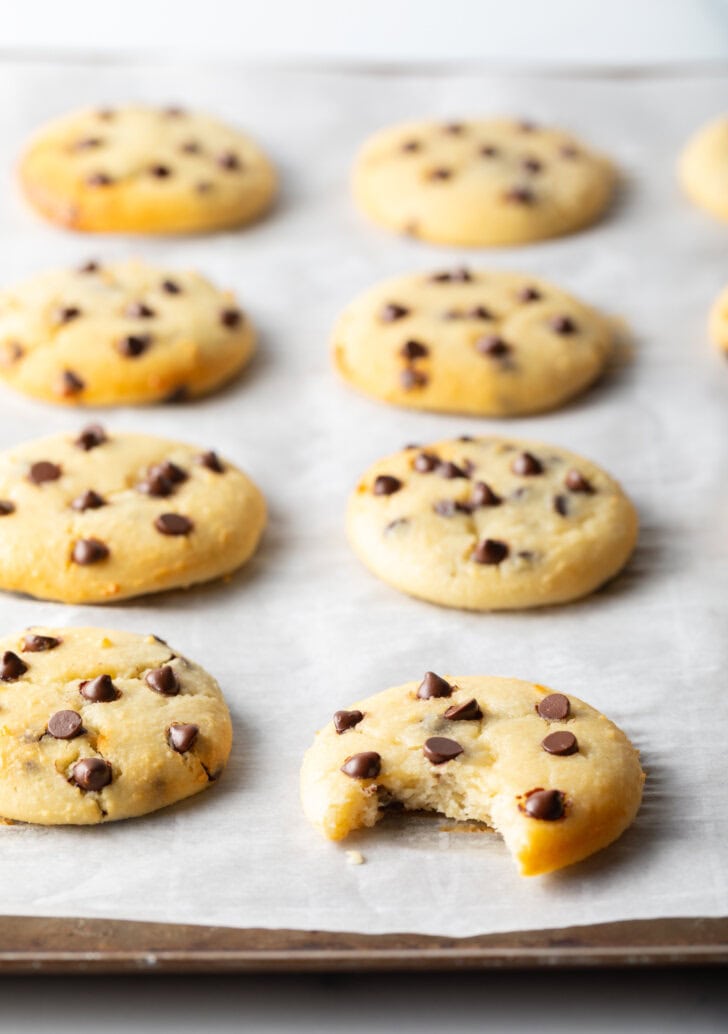 8 cottage cheese chocolate chip cookies cooling on a baking sheet. A front cookie has a bite missing.