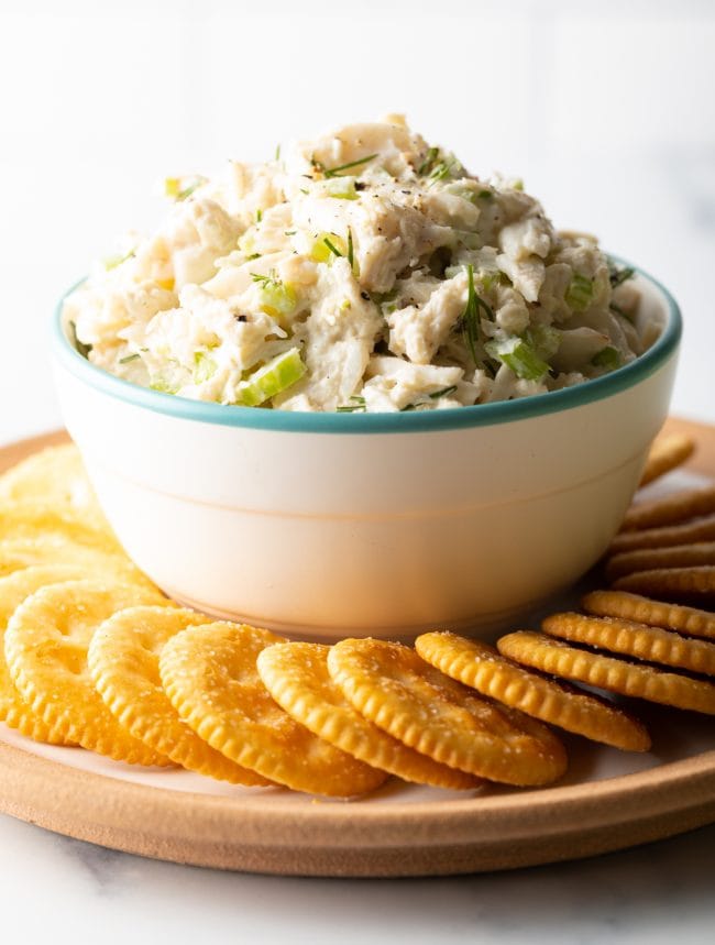 Bowl of real crab salad on top of a serving dish with crackers on it. 