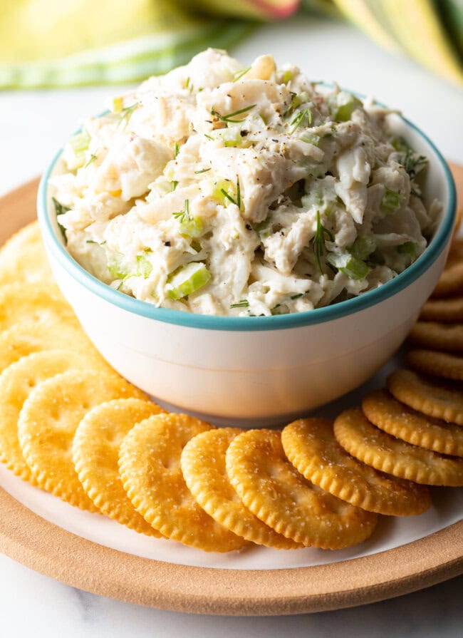 a bowl of seafood salad with chopped celery and dill with crackers