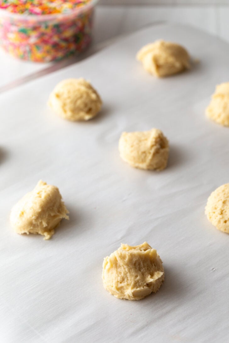 Several raw cookie dough balls on a baking sheet.