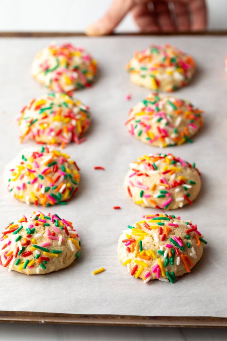 8 cream cheese cookies on a baking sheet, each topped with sprinkles.