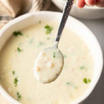 Top down view white bowl with creamy chicken soup garnished with fresh parsley. A metal spoon has a spoonful showing to camera.