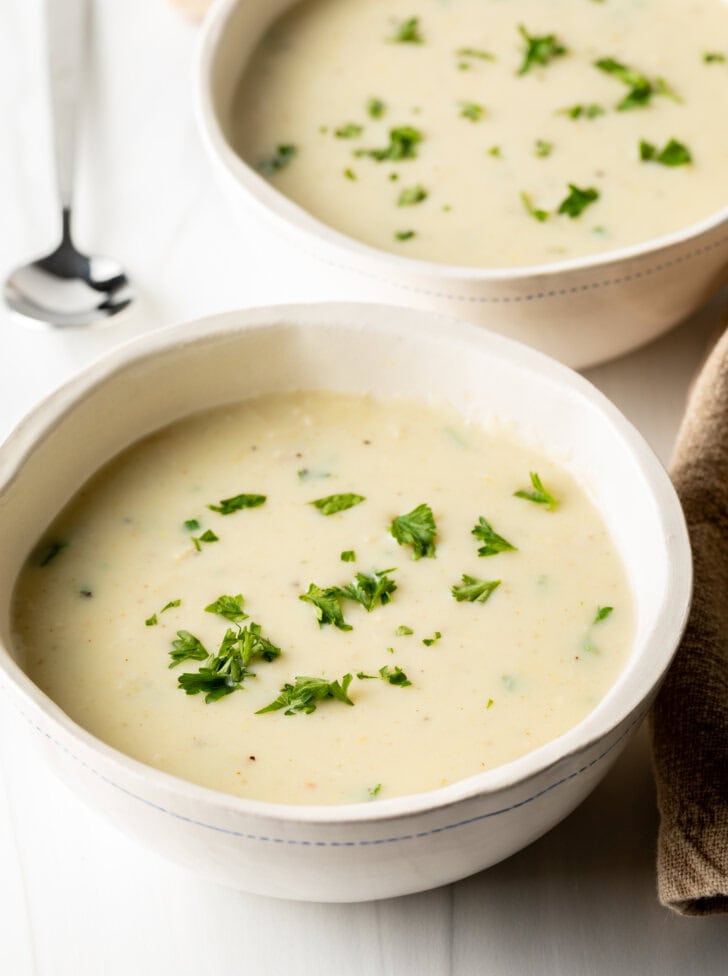 Two white bowls with cream of chicken soup, garnished with fresh chopped parsley.