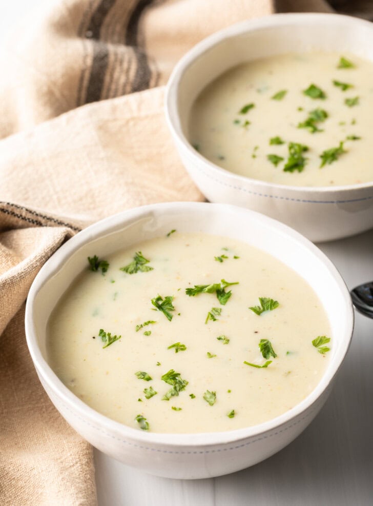 Two white bowls with cream of chicken soup, garnished with fresh chopped parsley.