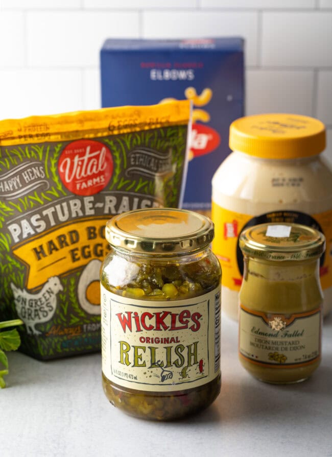 Recipe ingredients in jars including relish, mustard, mayo, plus box of pasta and bag of hard boiled eggs.