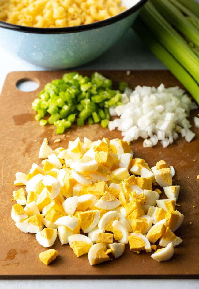 Cutting board with piles of chopped celery, onion, and eggs.