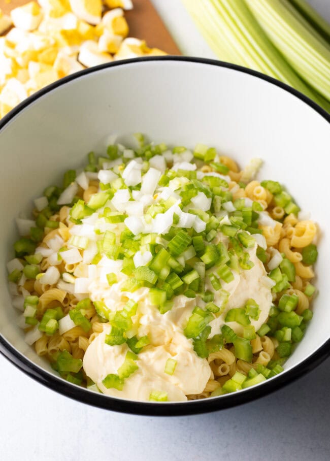 Adding mayo and celery to bowl with noodles.