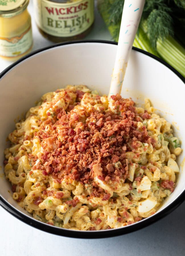 Noodles, chopped eggs, pickles, chopped bacon, and spices all together in a mixing bowl.