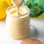 Spoon of dressing being held above a jar of tahini dressing.