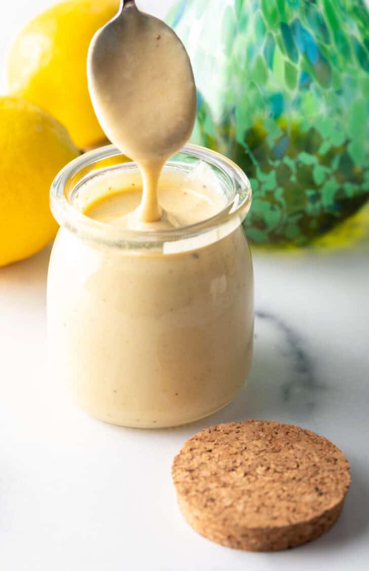 Spoon of dressing being held above a jar of tahini dressing.