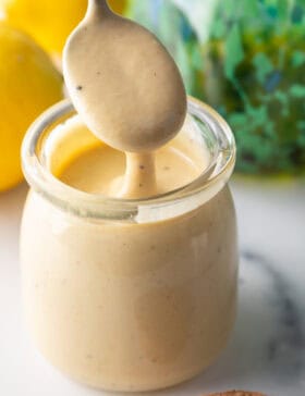 Spoon of dressing being held above a jar of tahini dressing.