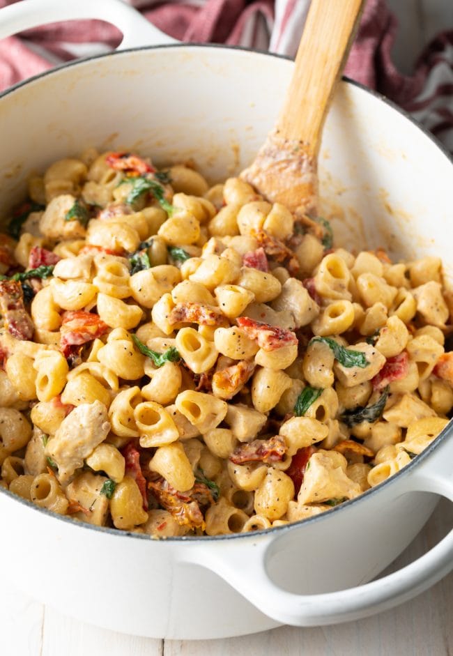 Creamy Chicken Tuscan Pasta - White pot of creamy macaroni noodles with chicken, sun dried tomatoes, and spinach.