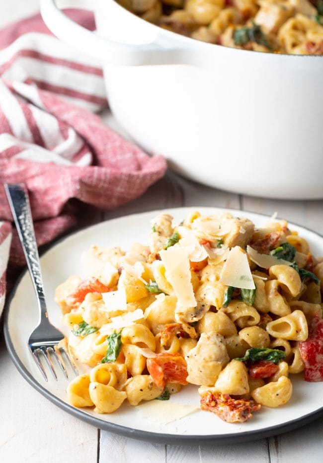 White plate of creamy tuscan chicken pasta with a fork on the side.