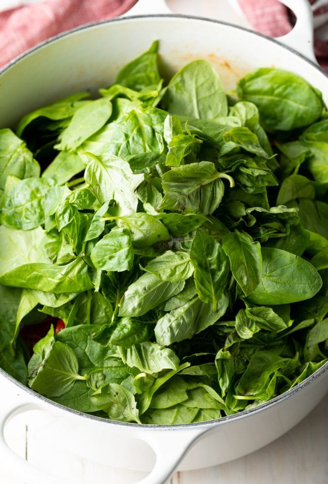 Spinach added to the white pot of tuscan chicken pasta.