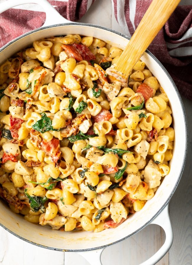 Overhead view of pot of creamy macaroni noodles with chicken, sun dried tomatoes, and spinach.