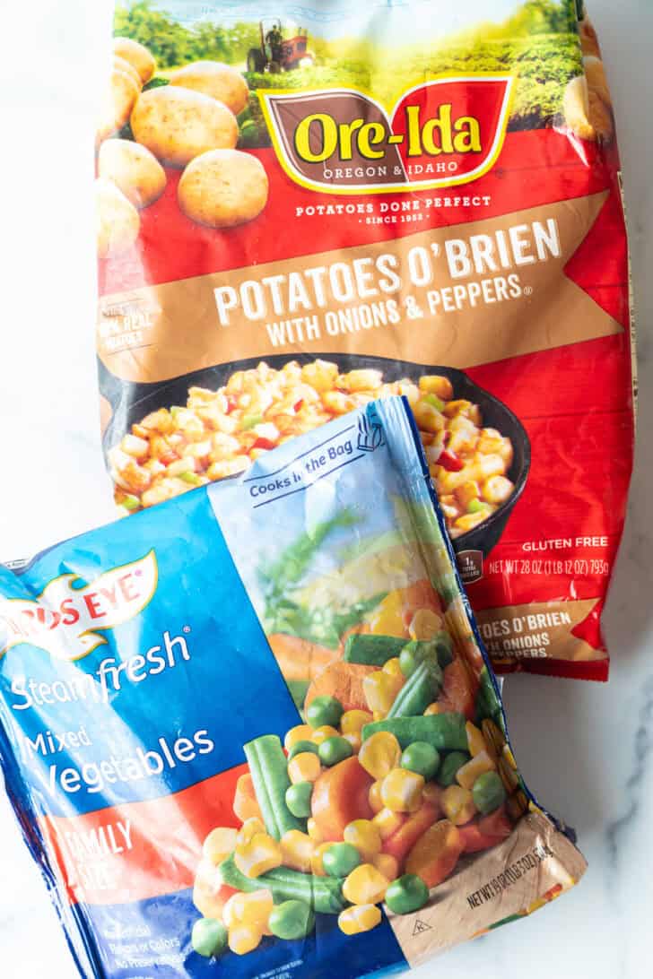 A bag of frozen potatoes o'brien and a bag of frozen mixed vegetables.