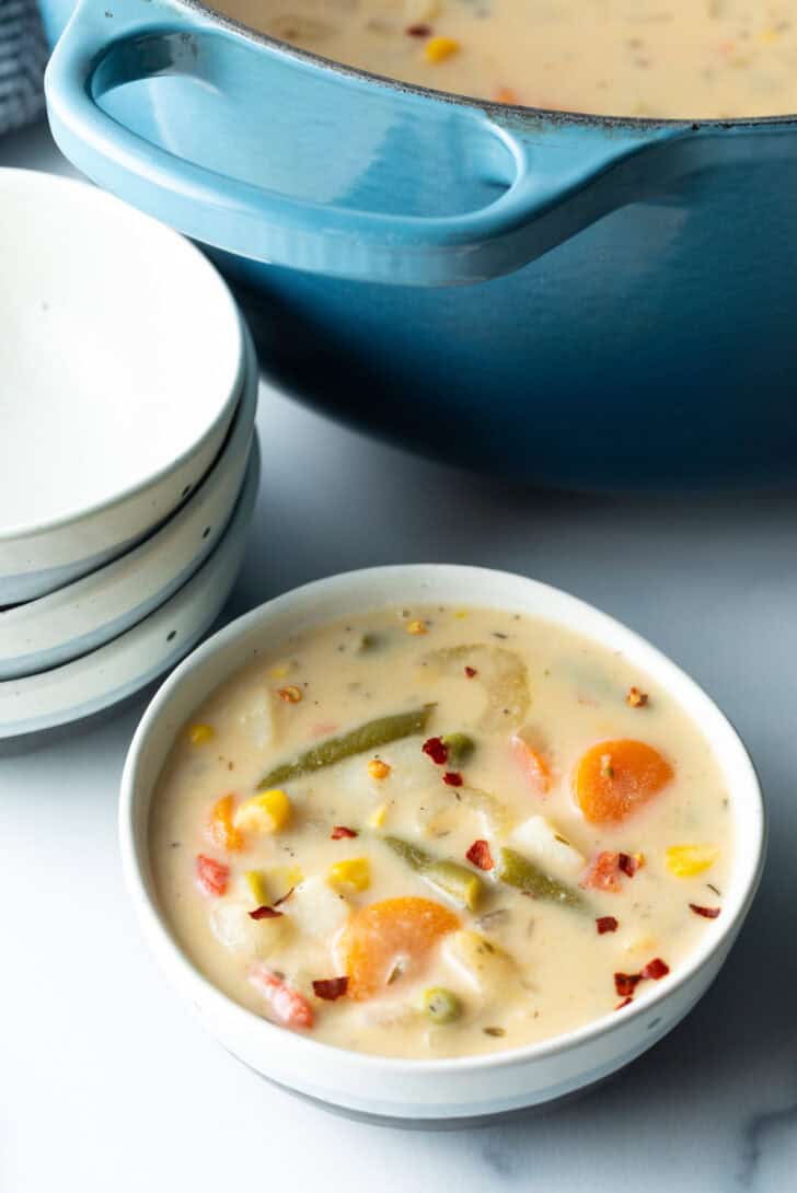 Top down bowl of creamy vegetable soup with carrots, green beans, corn, and potatoes.