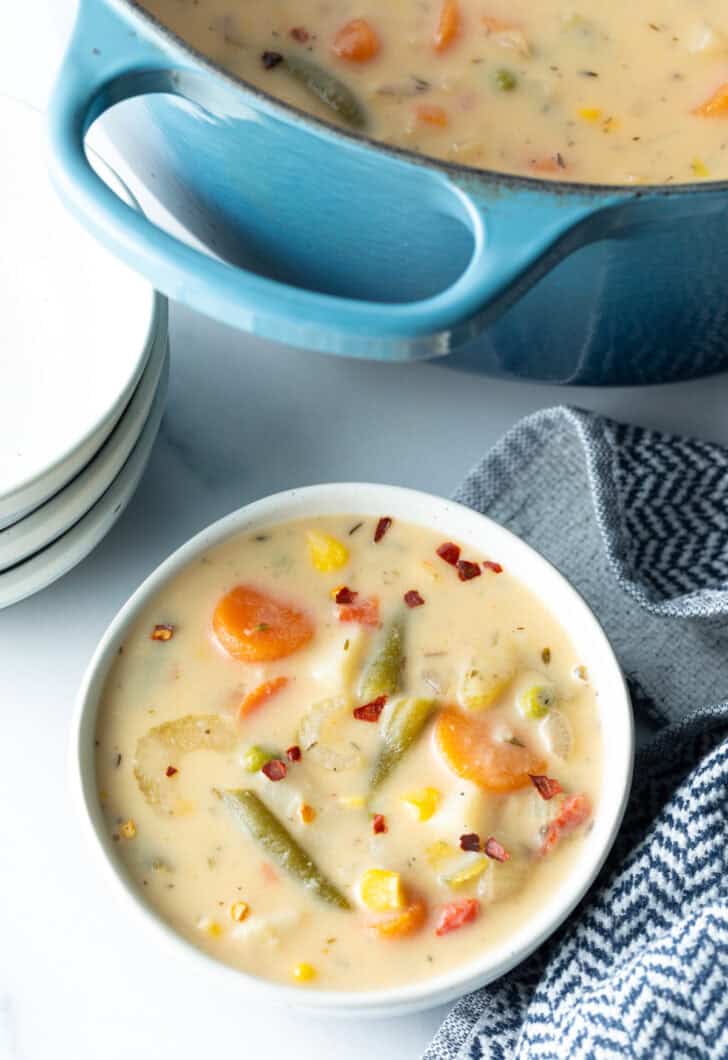 Top down bowl of creamy vegetable soup with carrots, green beans, corn, and potatoes.