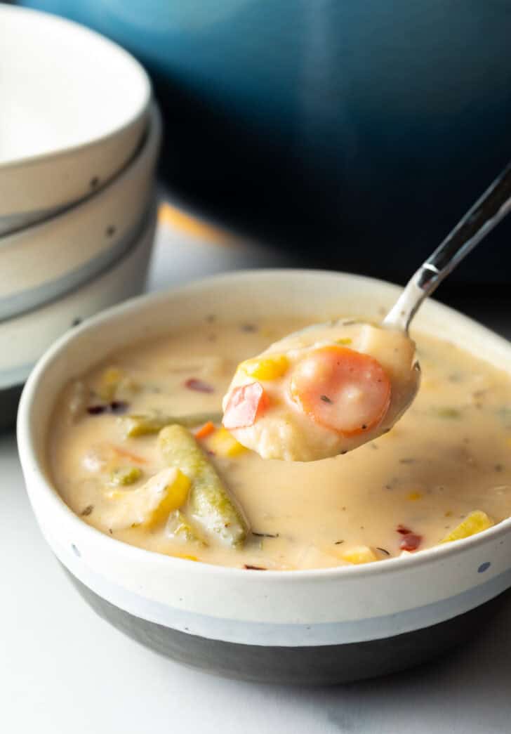 A bowl of cream veggie soup, with a spoon showing a scoop above the bowl.