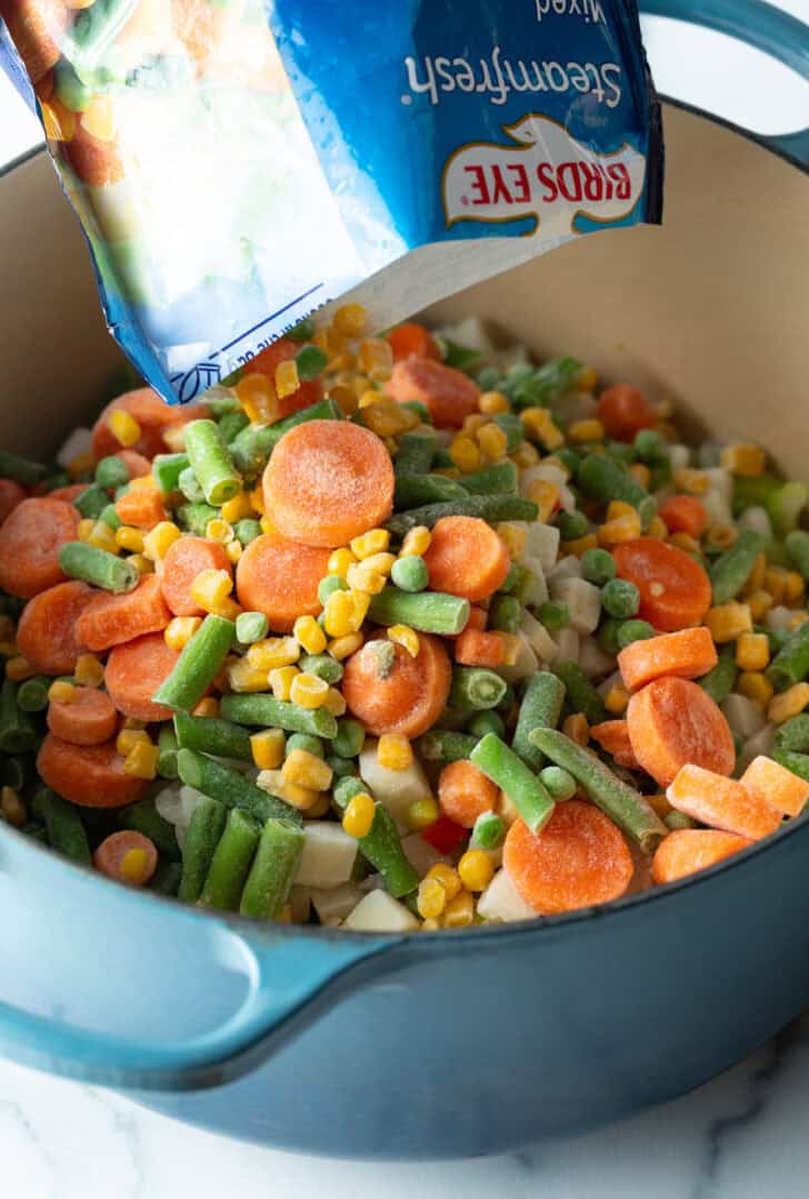 Pouring vegetable broth into a pot with frozen veggies.