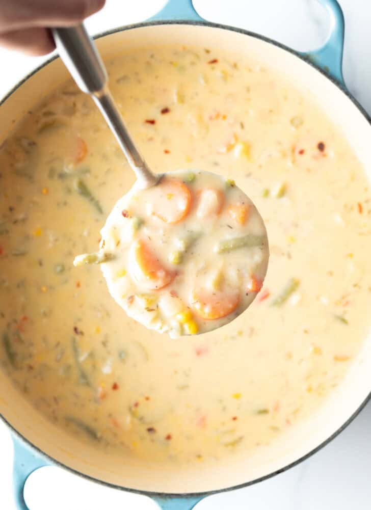 Large cooking pot with creamy vegetable soup, with a ladle showing a scoop to camera.