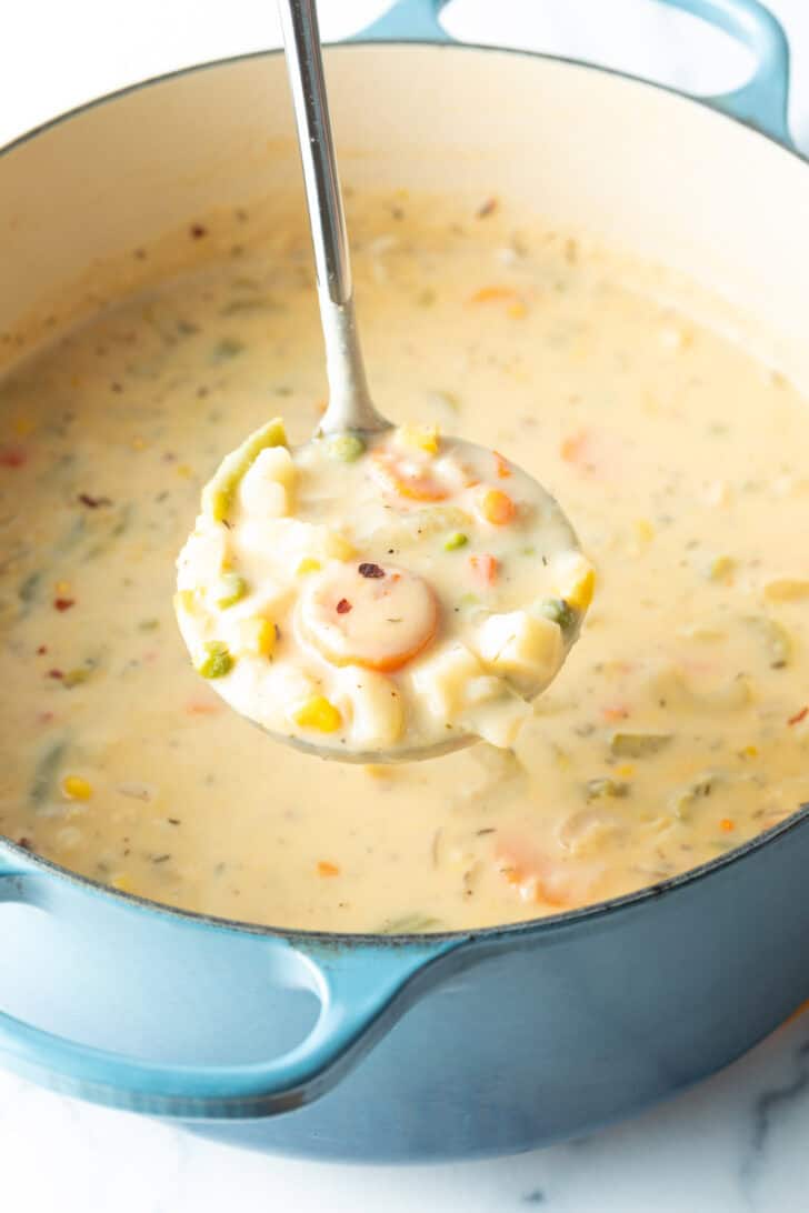 Large cooking pot with creamy vegetable soup, with a ladle showing a scoop to camera.