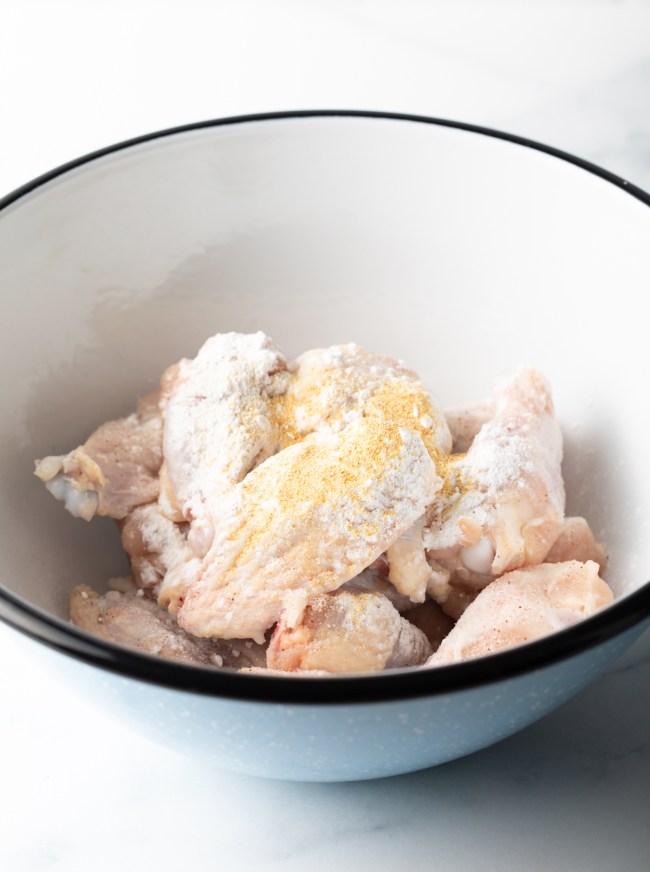 Raw wings in a white mixing bowl, covered in spices.