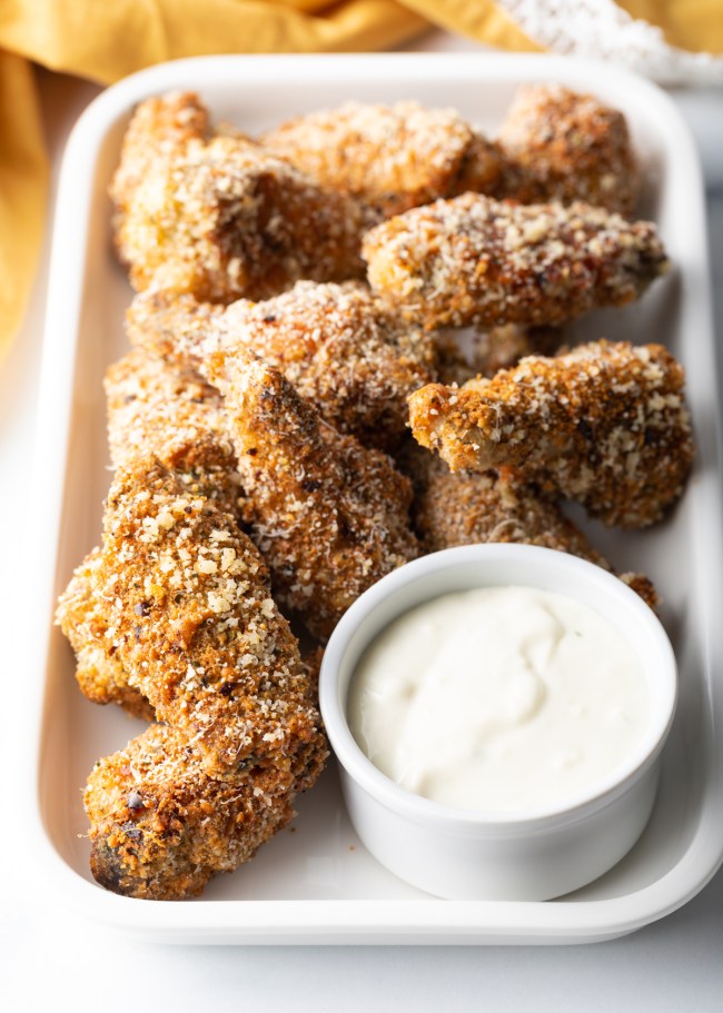 Serving of garlic parmesan wings on a white platter with white creamy sauce.