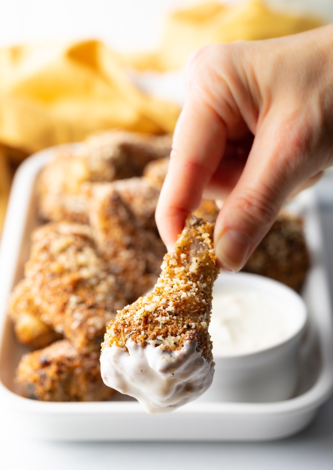 Hand holding parmesan garlic wing dipped in white sauce to the camera.