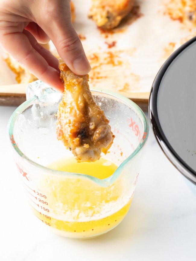 Hand dipping a wing into glass measuring cup with melted butter.