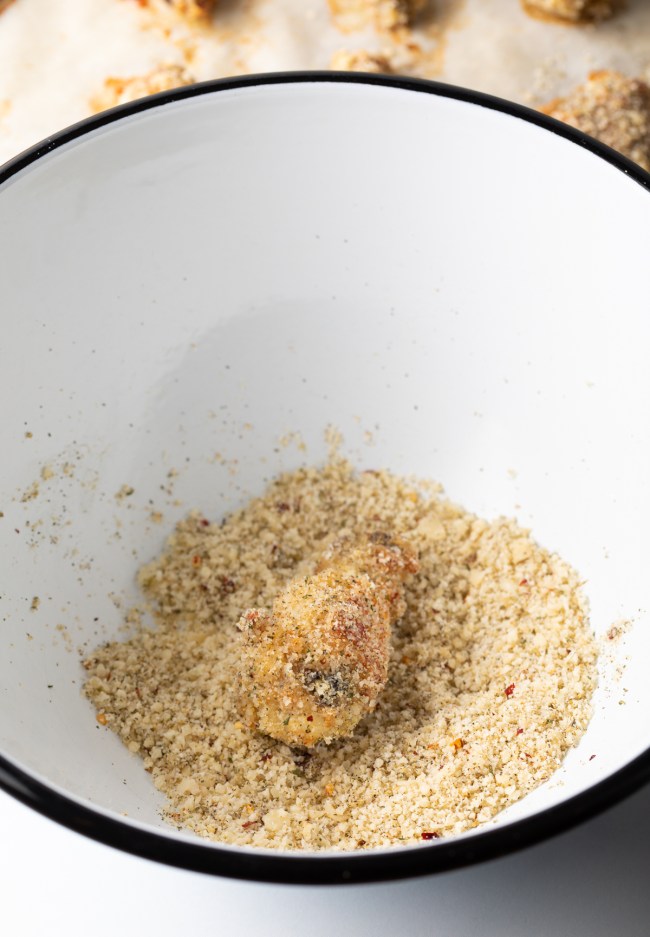 Wing being tossed with parmesan cheese and spice mixture in a large white bowl.
