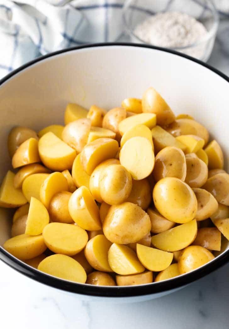 Large white bowl of halved yellow potatoes.