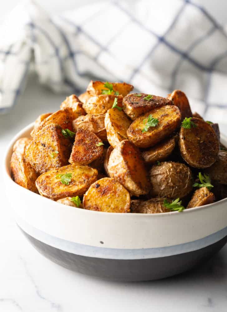 Bowl of crispy oven roasted potatoes sprinkled with fresh parsley.