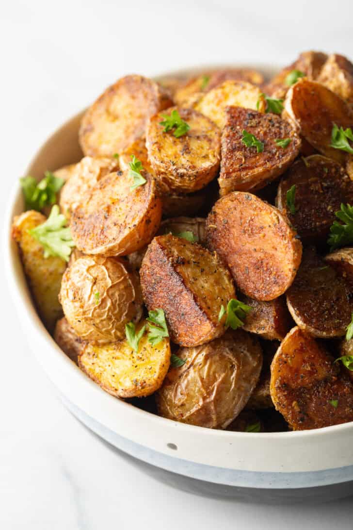 Bowl of crispy oven roasted potatoes sprinkled with fresh parsley.