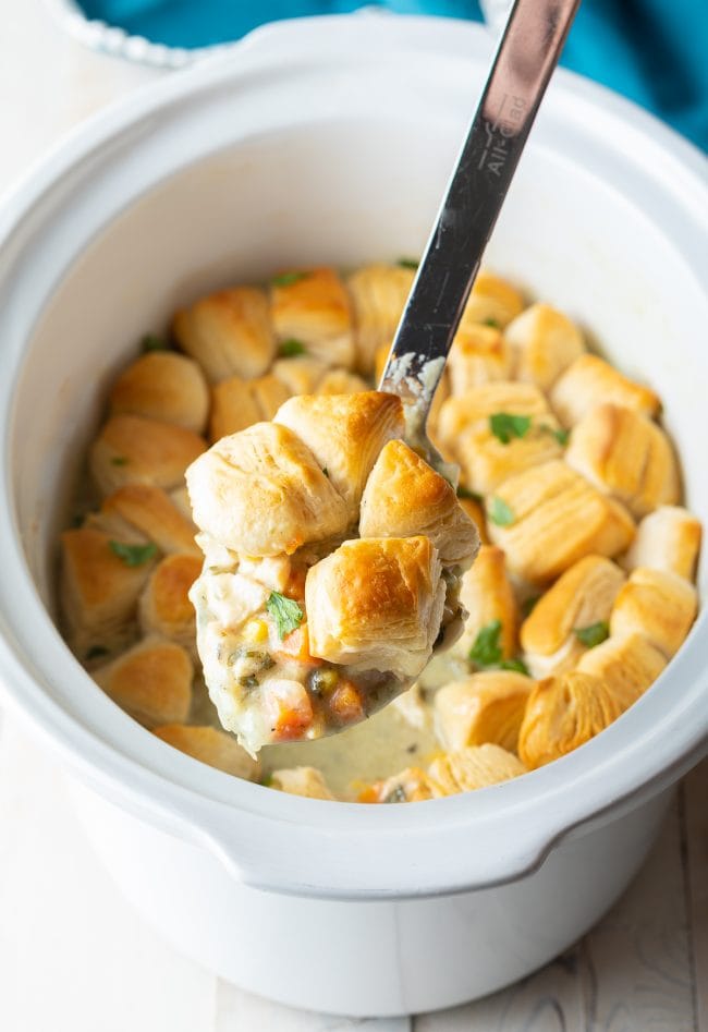 Spoonful of chicken pot pie filling with biscuit pieces and more in the background. 